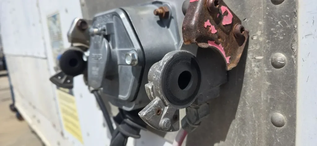 Close-up of a worn black rubber glad hand seal next to a heavily rusted and corroded steel mounting bracket on a commercial trailer air brake fitting