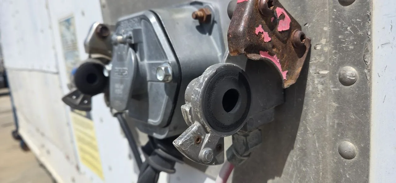 Worn glad hand seal with corroded mounting bracket on semi-truck trailer Close-up of a worn black rubber glad hand seal next to a heavily rusted and corroded steel mounting bracket on a commercial trailer air brake fitting