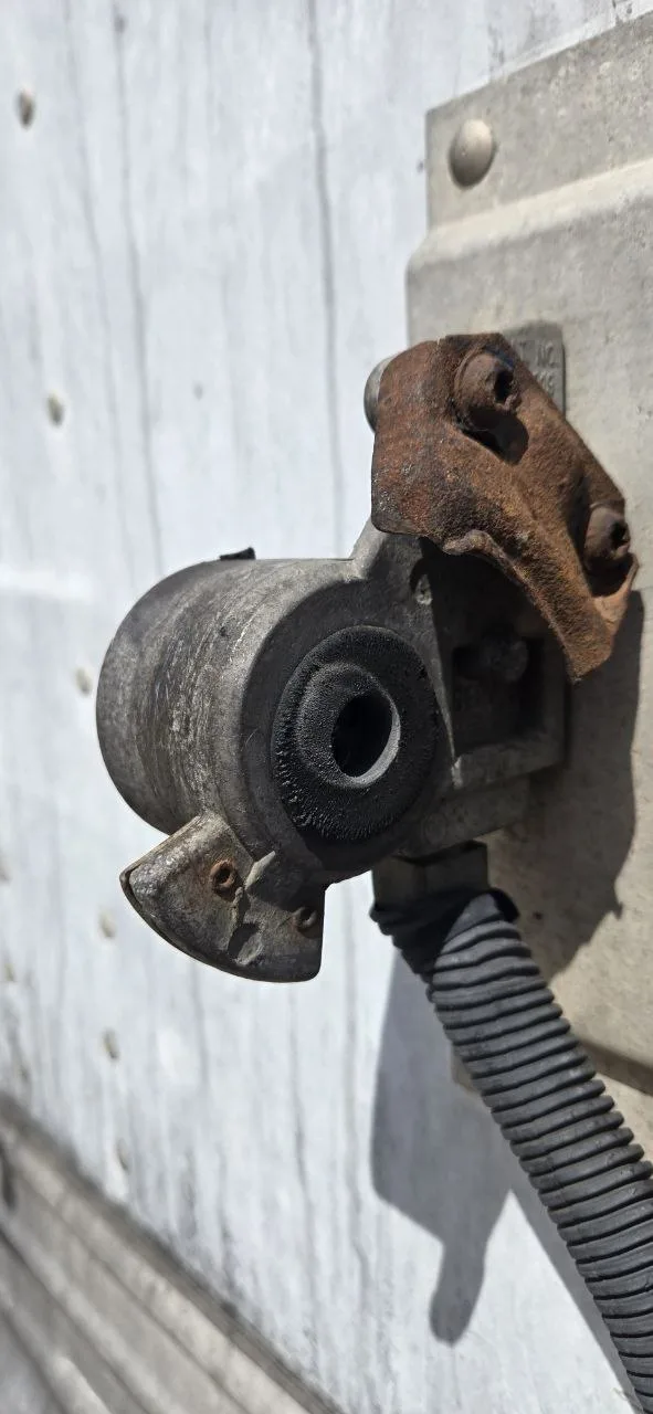 Rusted glad hand mounting bracket close-up on trailer air brake line Close-up vertical view of a rusted and flaking mounting bracket holding a glad hand air brake seal on a semi trailer, showing exposed corrosion around the bolt holes